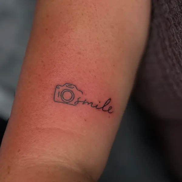 Kruopšti minimalistinė fotoaparato ir šypsenos tatuiruotė